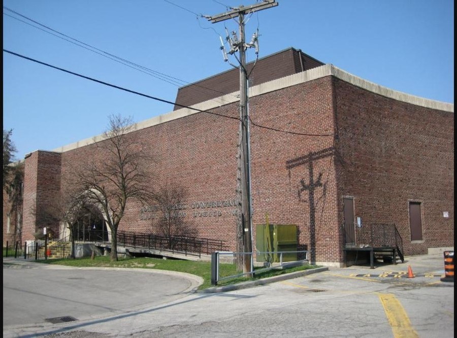 A red brick synagogue building on a Toronto street corner, with an inscribed stone lintel above the entrance and a utility pole in front.