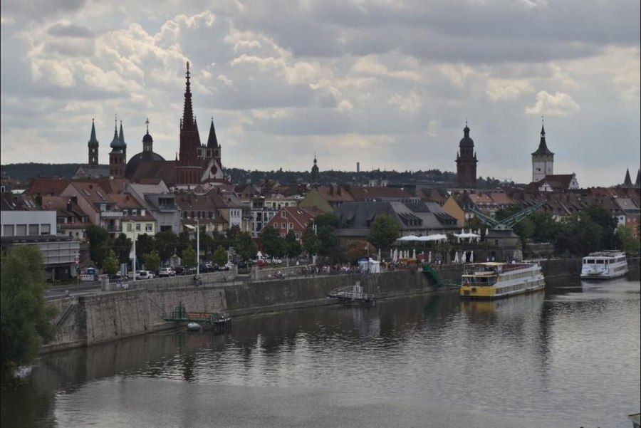 A panoramic view of Würzburg's old town along the Main river, with church spires and a hilltop fortress visible above the rooftops.